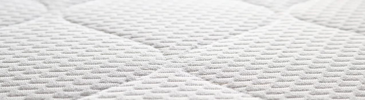 Imagem da superfície de um colchão branco com detalhes de costura no formato de losango.