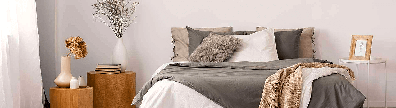 Quarto com paredes brancas com cama de casal no centro com cobertores e travesseiros na cor cinza. Quarto com paredes brancas com cama de casal no centro com cobertores e travesseiros na cor cinza.
