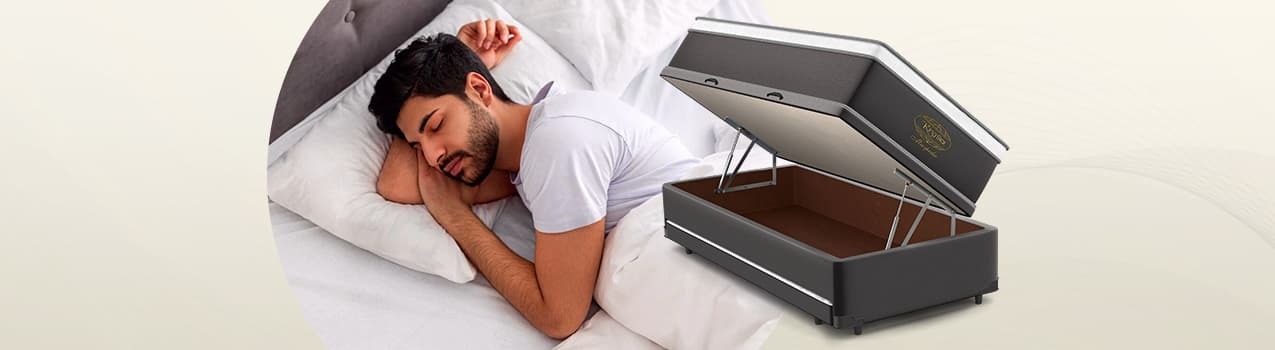 Imagem de homem caucasiano dormindo em cama à esquerda e, à direita, um modelo de bicama com baú da King Star aberto. Imagem de homem caucasiano dormindo em cama à esquerda e, à direita, um modelo de bicama com baú da King Star aberto.